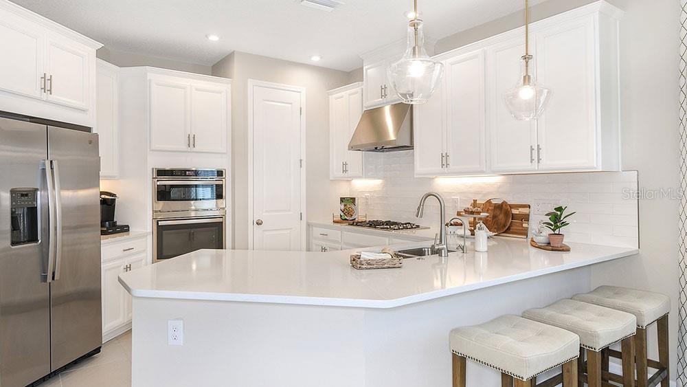 A modern kitchen features white cabinetry, stainless steel appliances, a quartz island, and pendant lighting — 763 STEEL DRIVE, APOLLO BEACH, FL