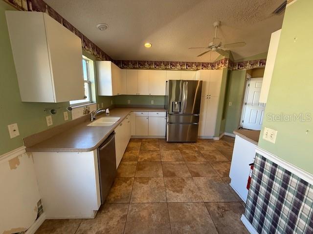 A kitchen features white cabinets, stainless steel appliances, tan tile flooring, and green walls — 17760 SE 91ST FREEDOM COURT, THE VILLAGES, FL
