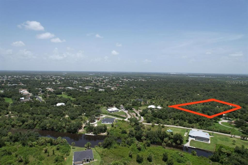 An aerial view shows a wooded lot outlined in red near a canal and houses — 1232 HARBOUR SUNSET COURT, PUNTA GORDA, FL