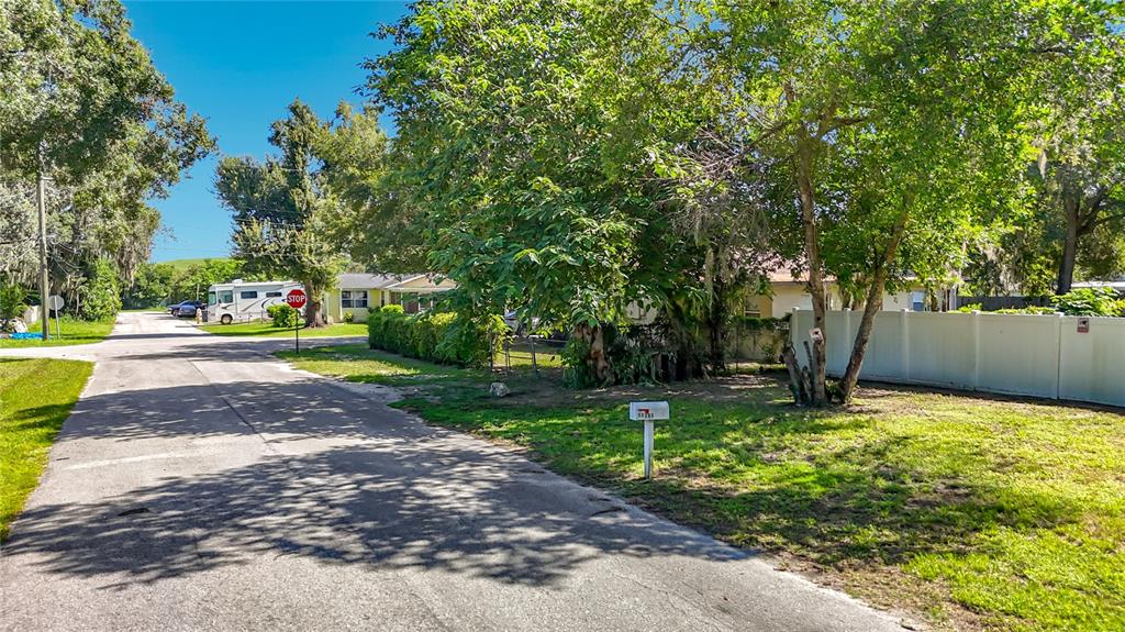 A residential street view featuring a white fence, mature trees, and a mailbox — 11707 CARVER ST, THONOTOSASSA, FL