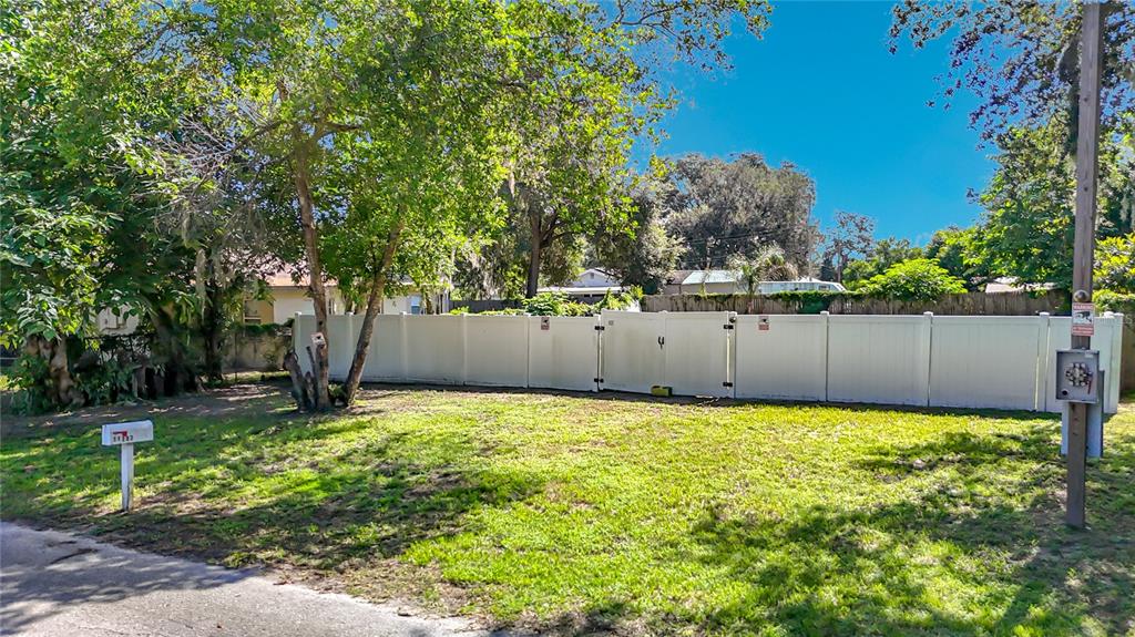 A white vinyl privacy fence encloses a grassy lot with trees and a mailbox — 11707 CARVER ST, THONOTOSASSA, FL