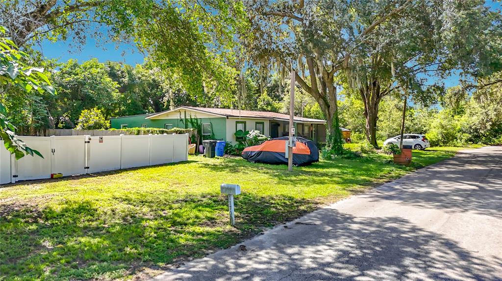 A single-story house with a white fence and a car covered by a tarp outside — 11707 CARVER ST, THONOTOSASSA, FL