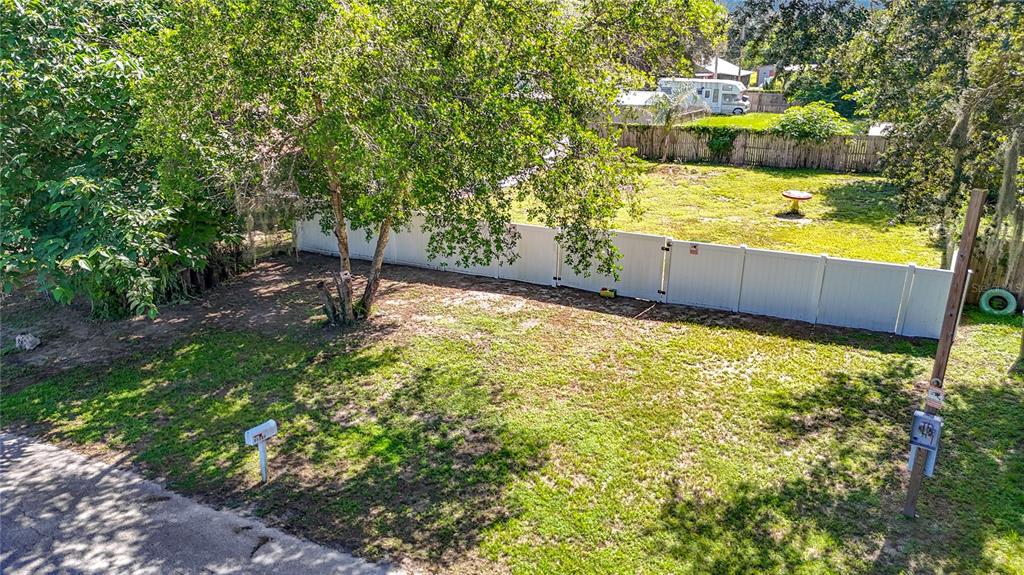 A grassy residential lot features a large tree, a white vinyl fence, and a mailbox — 11707 CARVER ST, THONOTOSASSA, FL