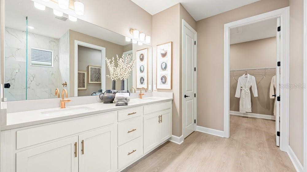 A modern bathroom features a double vanity with white cabinets, gold hardware, and a walk-in closet — 14236 DUNLIN AVENUE, PUNTA GORDA, FL