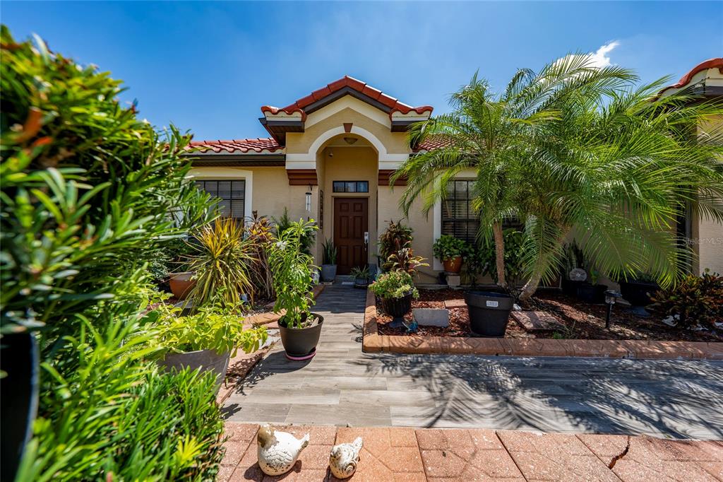 A front view of a house with a tiled walkway, potted plants, and a palm tree — 3012 VILLA PRECIOSA DRIVE, KISSIMMEE, FL