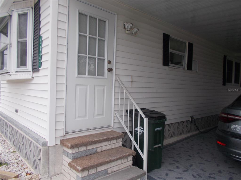 A white house exterior features a front door with stairs, a carport, and a trash bin — 6427 FLEETWOOD COURT, NORTH PORT, FL