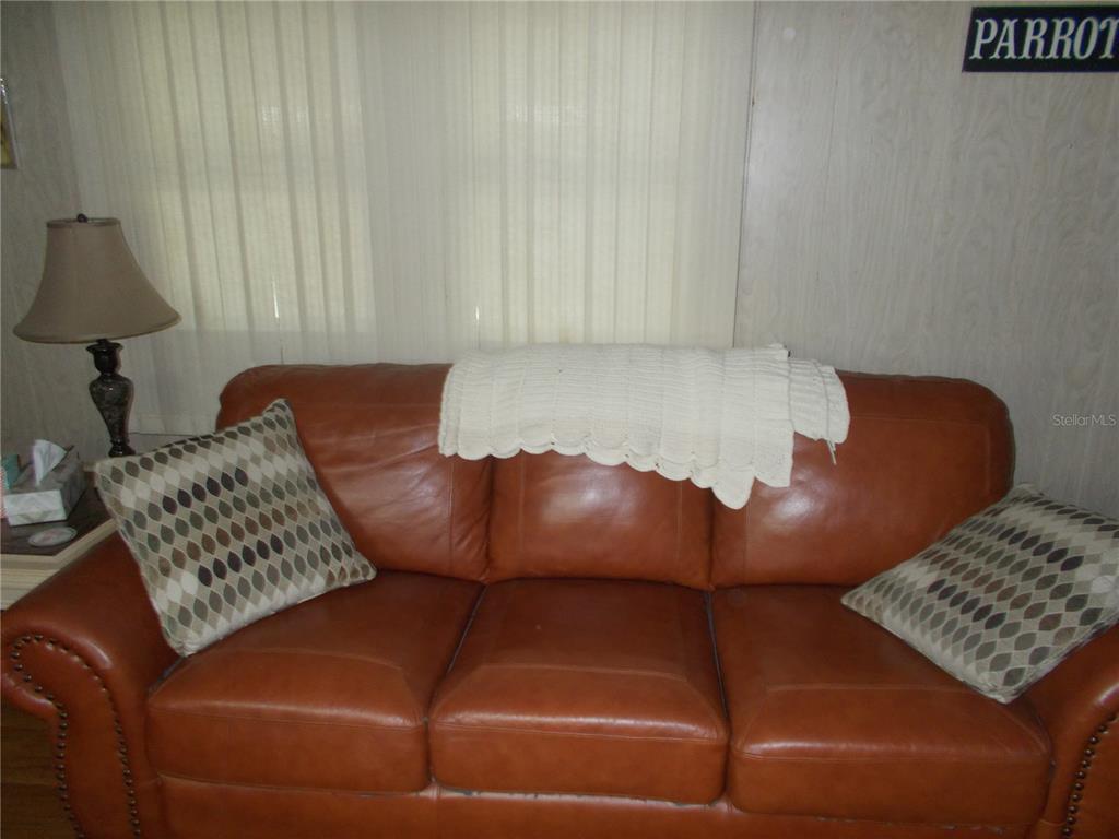 A brown leather sofa with two patterned pillows sits in front of vertical blinds — 6427 FLEETWOOD COURT, NORTH PORT, FL