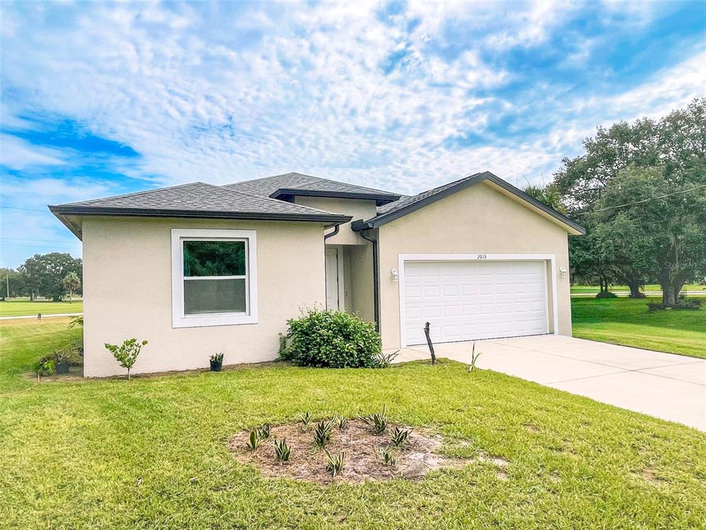 A single-story house with a beige stucco exterior, a two-car garage, and a front lawn — 2013 ODESSA CIRCLE, LABELLE, FL