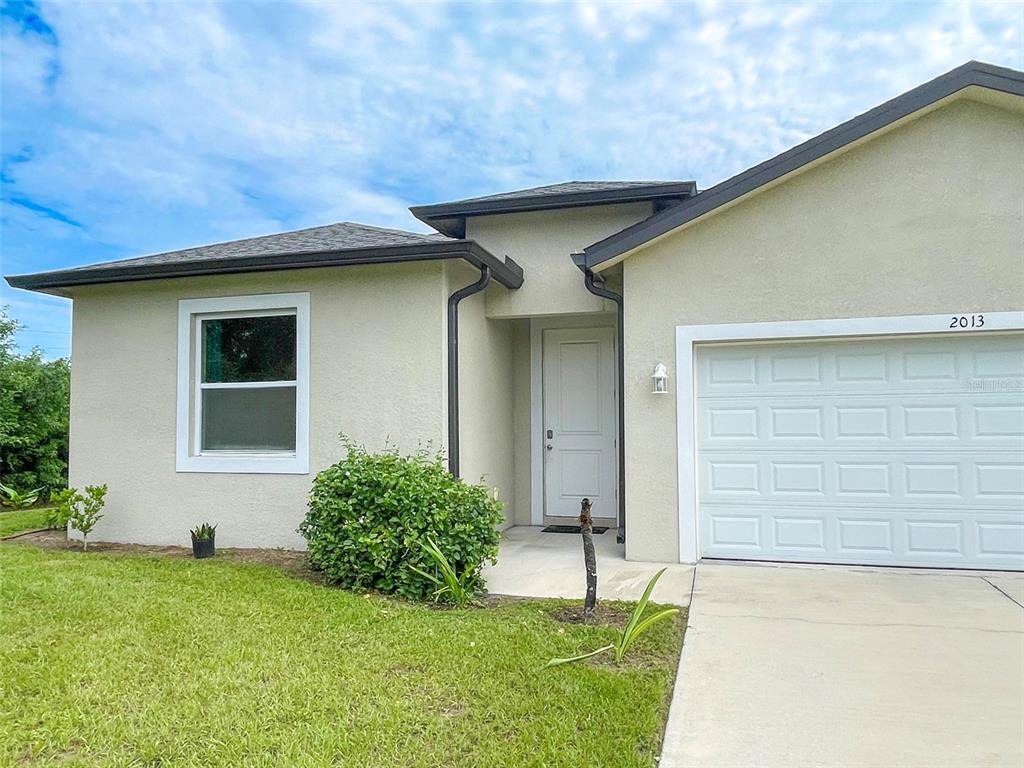 A single-story house exterior features a white garage door, a front entrance, and a window — 2013 ODESSA CIRCLE, LABELLE, FL
