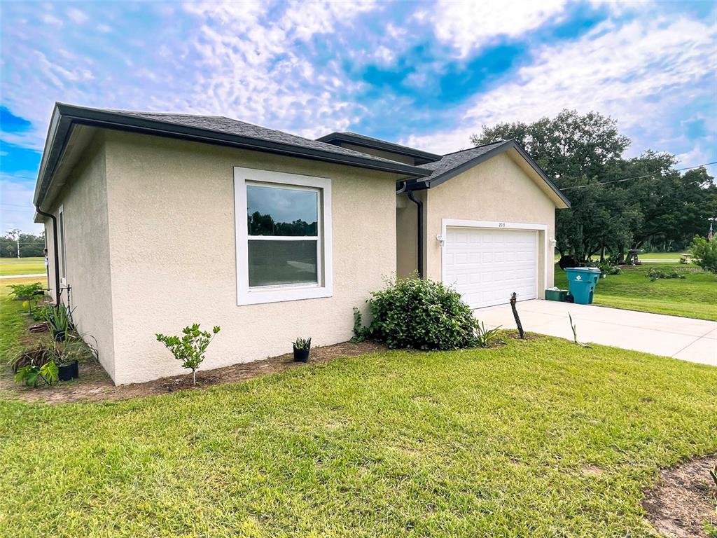 A single-story house with beige stucco siding, a white garage door, and a grassy lawn — 2013 ODESSA CIRCLE, LABELLE, FL
