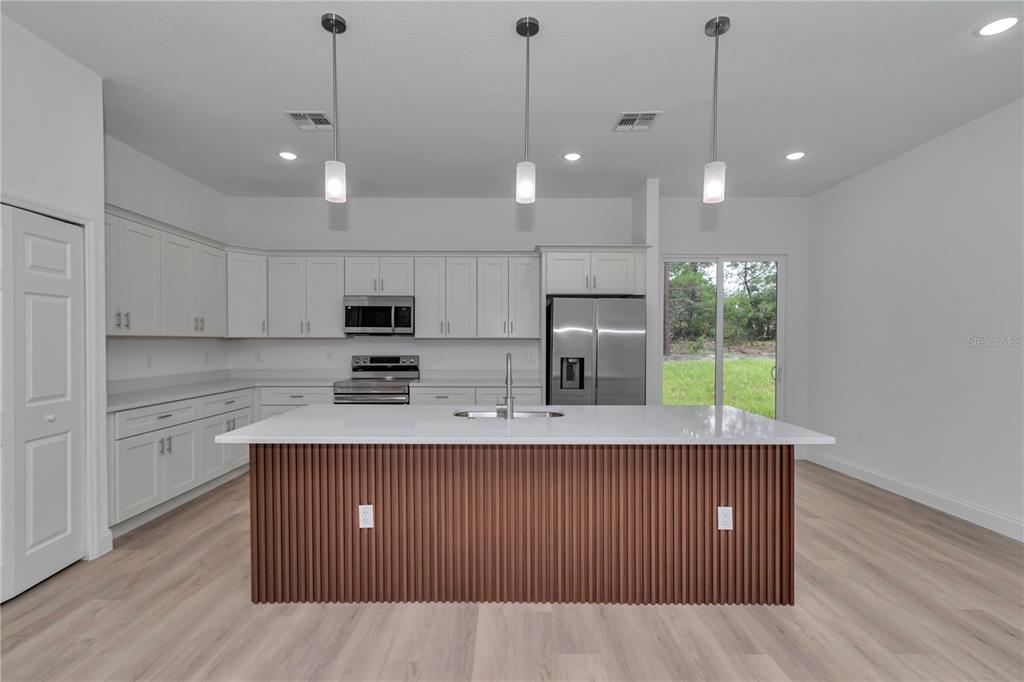 A modern kitchen features white cabinetry, a slatted wood island, and stainless steel appliances — 8737 N RAIDIN DRIVE, CITRUS SPRINGS, FL