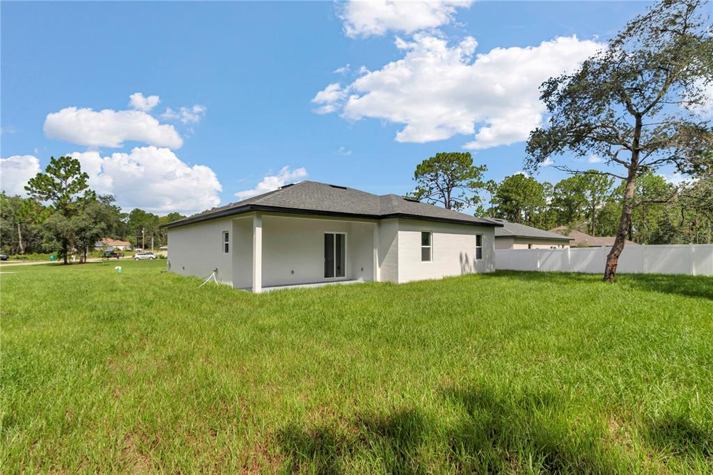 The rear exterior of a single-story house features a covered patio and a white fence — 8737 N RAIDIN DRIVE, CITRUS SPRINGS, FL