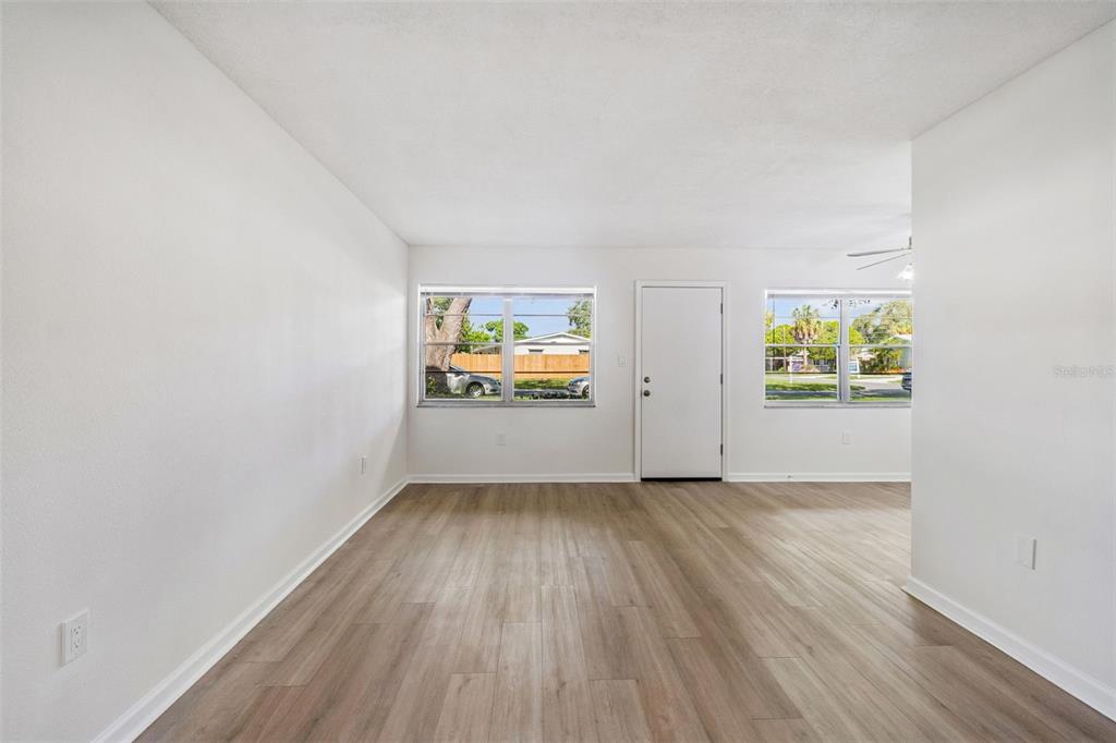 An empty living room features white walls, light wood-look flooring, and two windows — 8101 11TH STREET N UNIT 125, ST PETERSBURG, FL