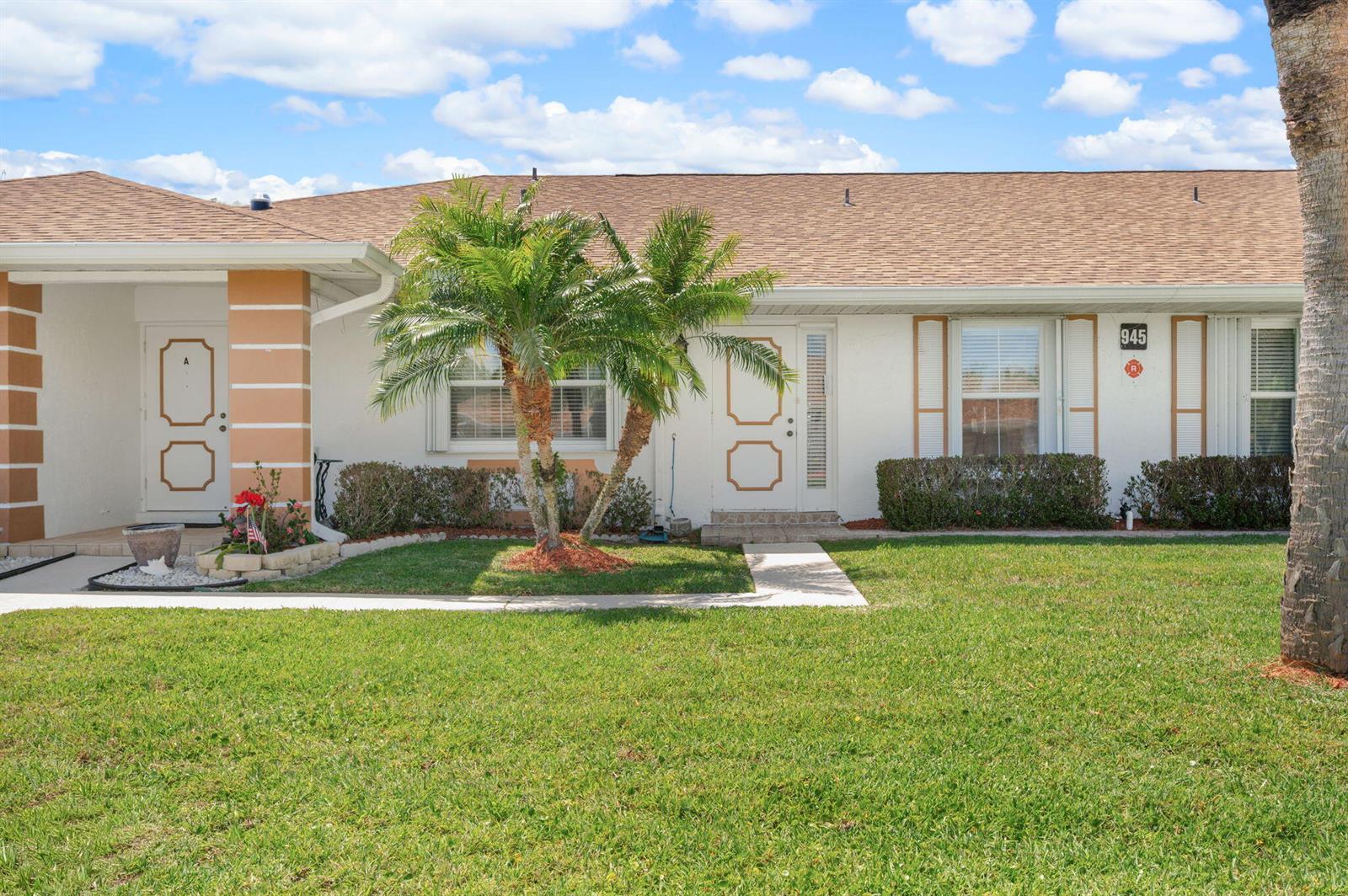 A single-story duplex with white stucco walls, a brown shingled roof, and a palm tree — 945 Savannas Point Drive # B, Fort Pierce FL 34982, FORT PIERCE, FL