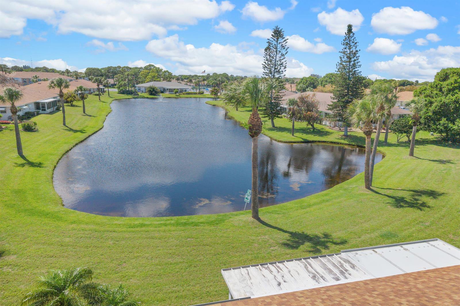 An aerial view shows a pond surrounded by green lawns, palm trees, and residential buildings — 945 Savannas Point Drive # B, Fort Pierce FL 34982, FORT PIERCE, FL