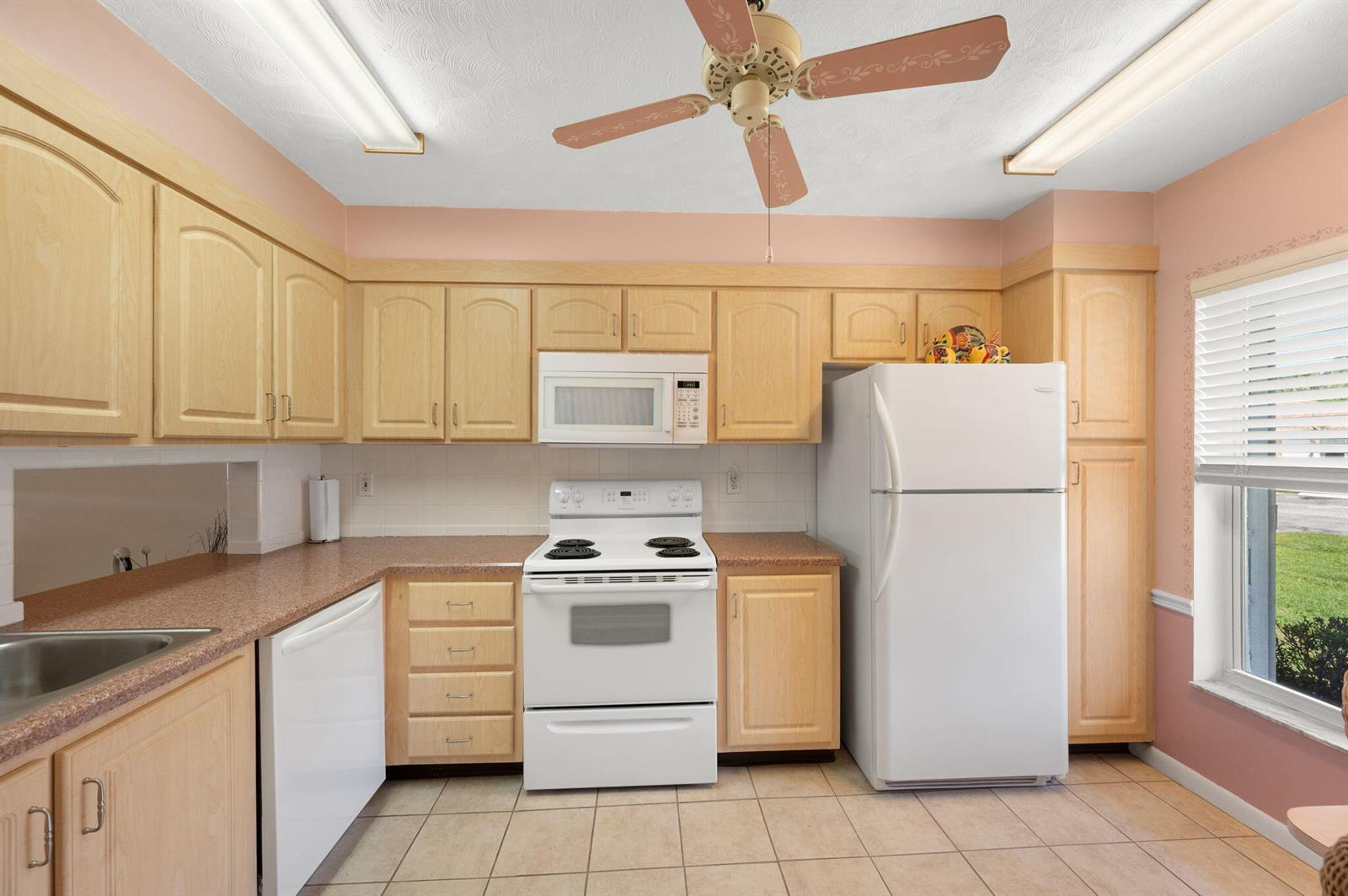 A kitchen features light wood cabinets, white appliances, pink walls, and a ceiling fan — 945 Savannas Point Drive # B, Fort Pierce FL 34982, FORT PIERCE, FL