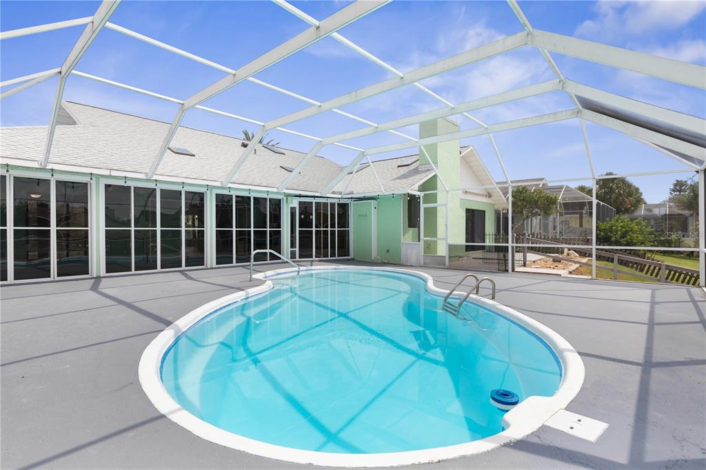 A swimming pool enclosed by a screened lanai sits on a gray patio behind a house — 6 CHERRY COURT, PALM COAST, FL