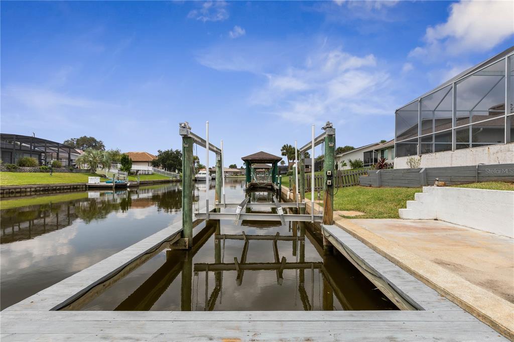 A boat lift sits in a canal behind a house with a screened-in patio — 6 CHERRY COURT, PALM COAST, FL