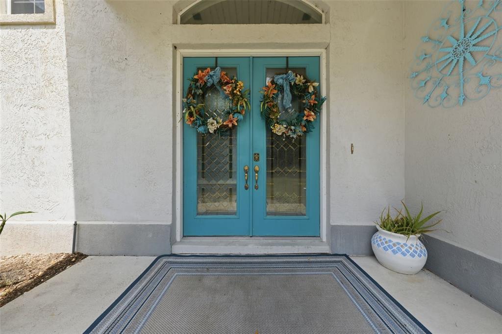A front entryway features double teal doors with glass panels and matching floral wreaths — 10639 SE SUNSET HARBOR ROAD, SUMMERFIELD, FL