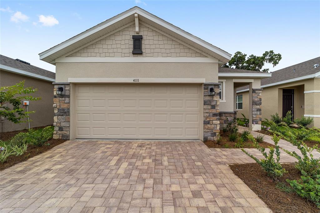 A single-story house exterior features a beige garage, stone accents, and a paved driveway — 4111 NW 44TH CIRCLE, OCALA, FL