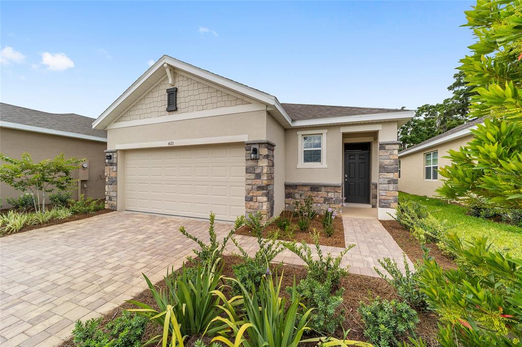A single-story house with a beige stucco exterior, stone accents, and a paved driveway — 4111 NW 44TH CIRCLE, OCALA, FL