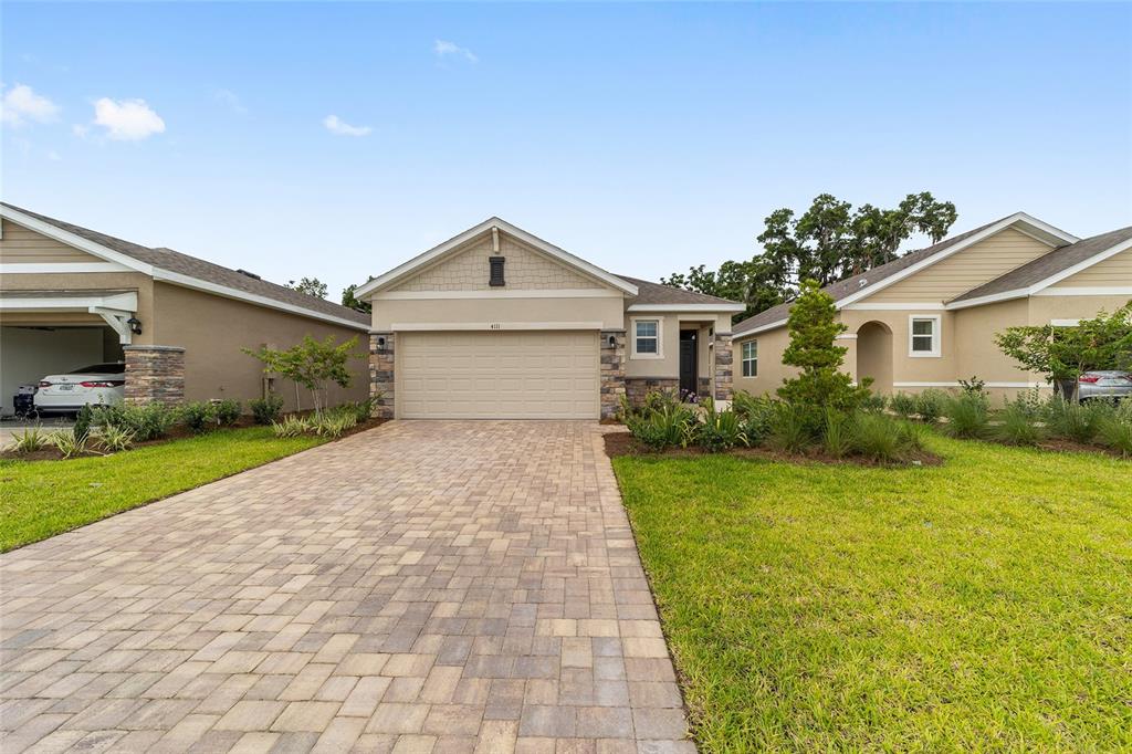 A single-story house with a beige garage, stone accents, and a paved driveway — 4111 NW 44TH CIRCLE, OCALA, FL