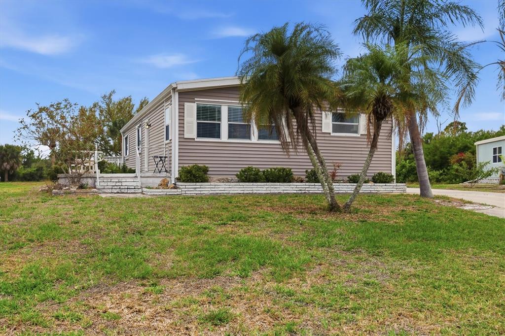 A single-story manufactured home with light gray siding sits on a grassy lot with palms — 3310 BLUE JAY LANE, ENGLEWOOD, FL