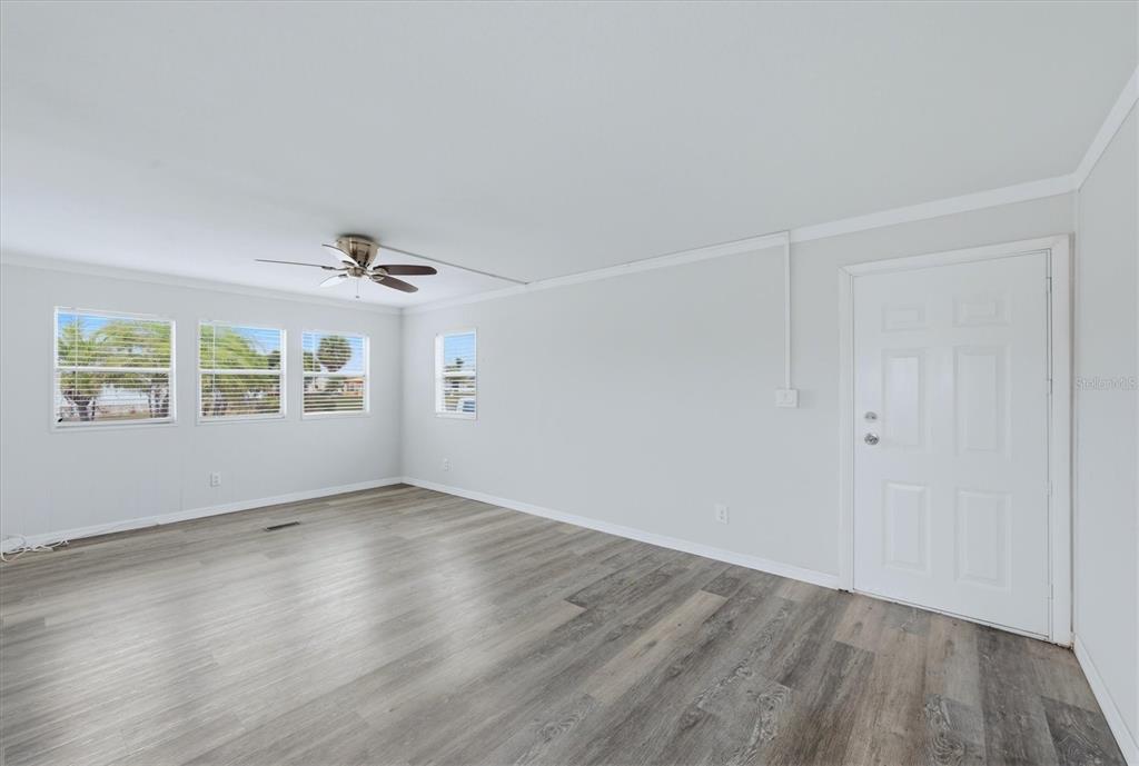 An empty room features light gray walls, wood-look flooring, a ceiling fan, and a white door — 3310 BLUE JAY LANE, ENGLEWOOD, FL
