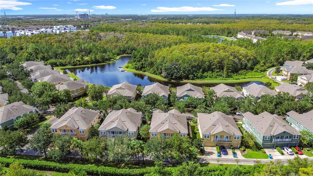 An aerial view shows a suburban neighborhood with houses surrounding a central pond and forest — 10338 LAKE DISTRICT LANE UNIT S, ORLANDO, FL