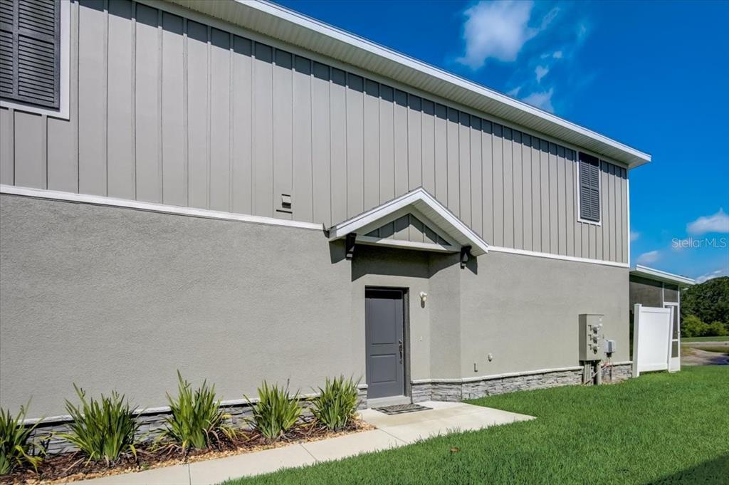 A gray exterior wall features a dark door under a small gable roof overhang — 10916 QUICKWATER COURT, RIVERVIEW, FL