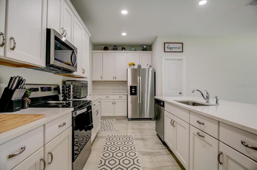 A modern kitchen features white cabinetry, stainless steel appliances, and a central island with sink — 10916 QUICKWATER COURT, RIVERVIEW, FL