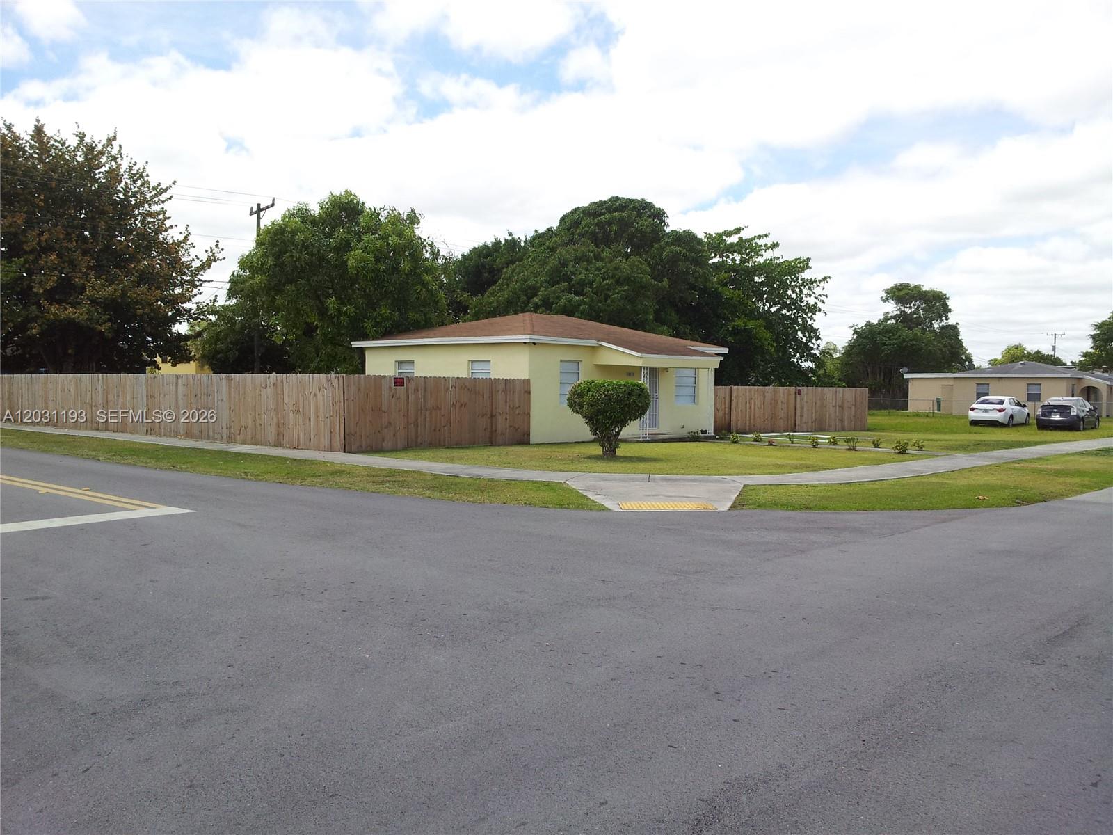 A yellow single-story house sits on a corner lot behind a wooden privacy fence — MIAMI, FL