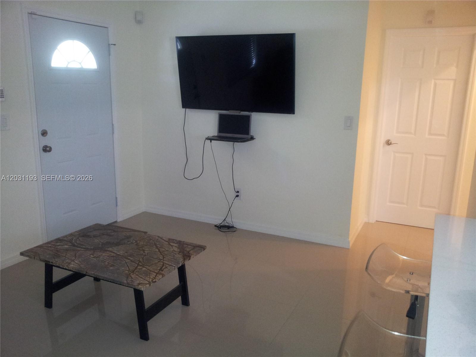 A living room features a wall-mounted television, a small laptop shelf, and a marble coffee table — MIAMI, FL