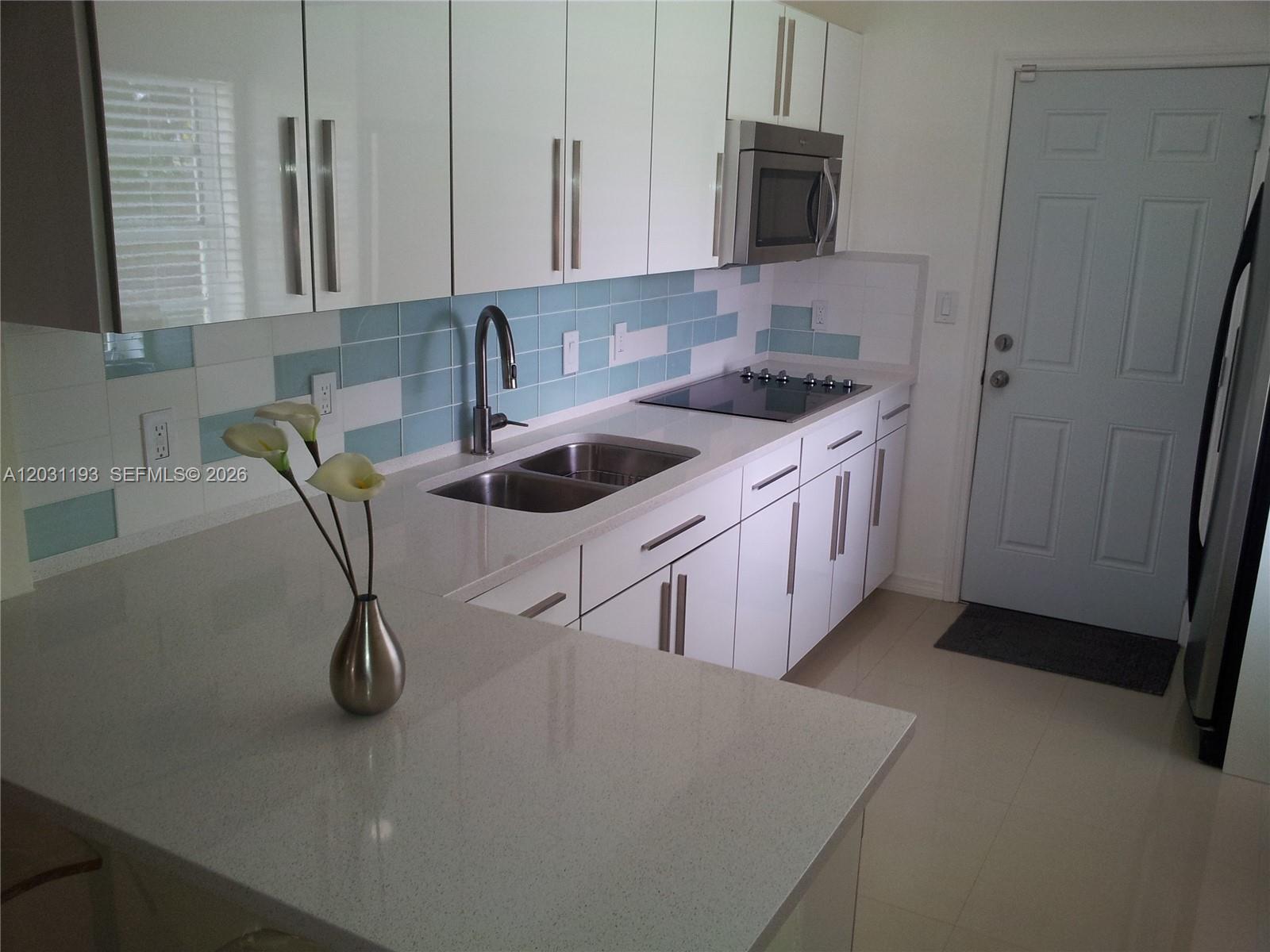 A modern kitchen features white cabinets, quartz countertops, a blue tiled backsplash, and stainless appliances — MIAMI, FL