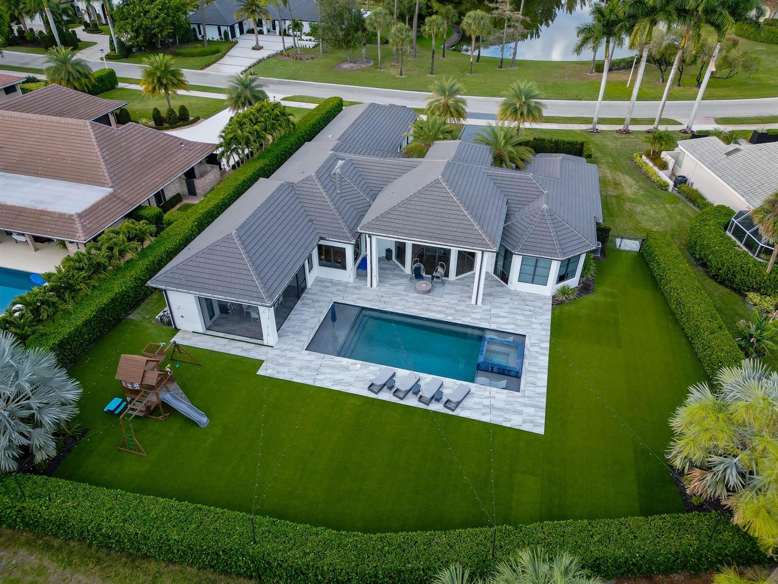 An aerial view shows a house with a gray tile roof, pool, and backyard lawn — 1768 Breakers West Boulevard W, West Palm Beach FL 33411, WEST PALM BEACH, FL