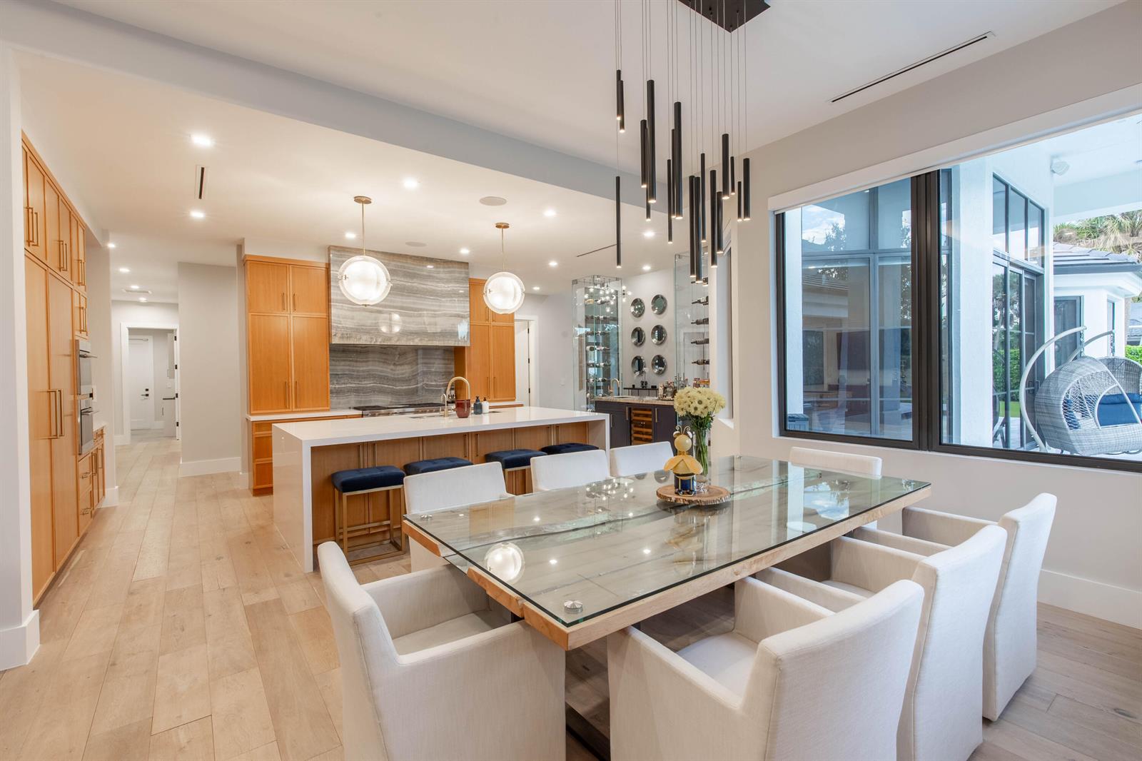 A modern kitchen and dining area features light wood cabinetry, a glass-topped table, and pendant lighting — 1768 Breakers West Boulevard W, West Palm Beach FL 33411, WEST PALM BEACH, FL