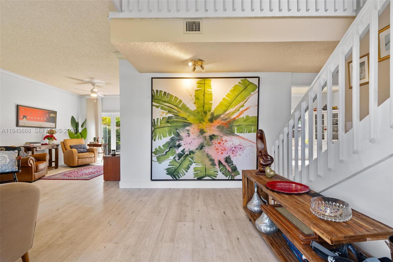 A bright living area features light wood flooring, a large palm leaf painting, and stairs — 4471 SW 154th Ct, Miami FL 33185, MIAMI, FL