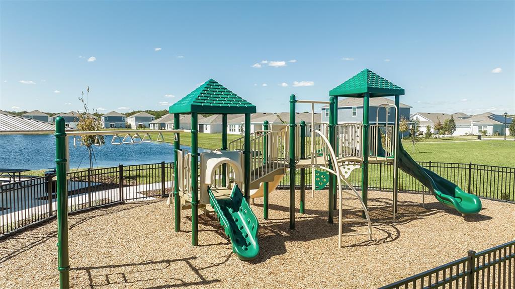 A playground with slides and climbing structures sits in a fenced area near a pond — 5431 ISLA SAONA DRIVE, KISSIMMEE, FL
