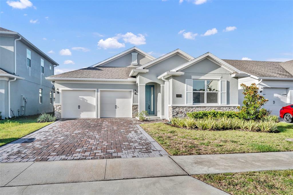 A single-story house with a two-car garage, stone accents, and a paved driveway — 19268 ALLIUM PLACE, ORLANDO, FL