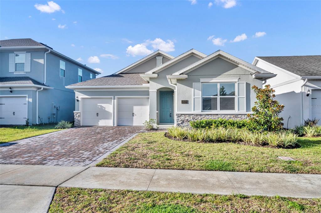 A single-story house with a two-car garage, stone accents, and a teal front door — 19268 ALLIUM PLACE, ORLANDO, FL