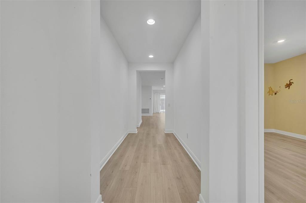 A hallway with light wood-look flooring leads to an open area with white walls — 19268 ALLIUM PLACE, ORLANDO, FL