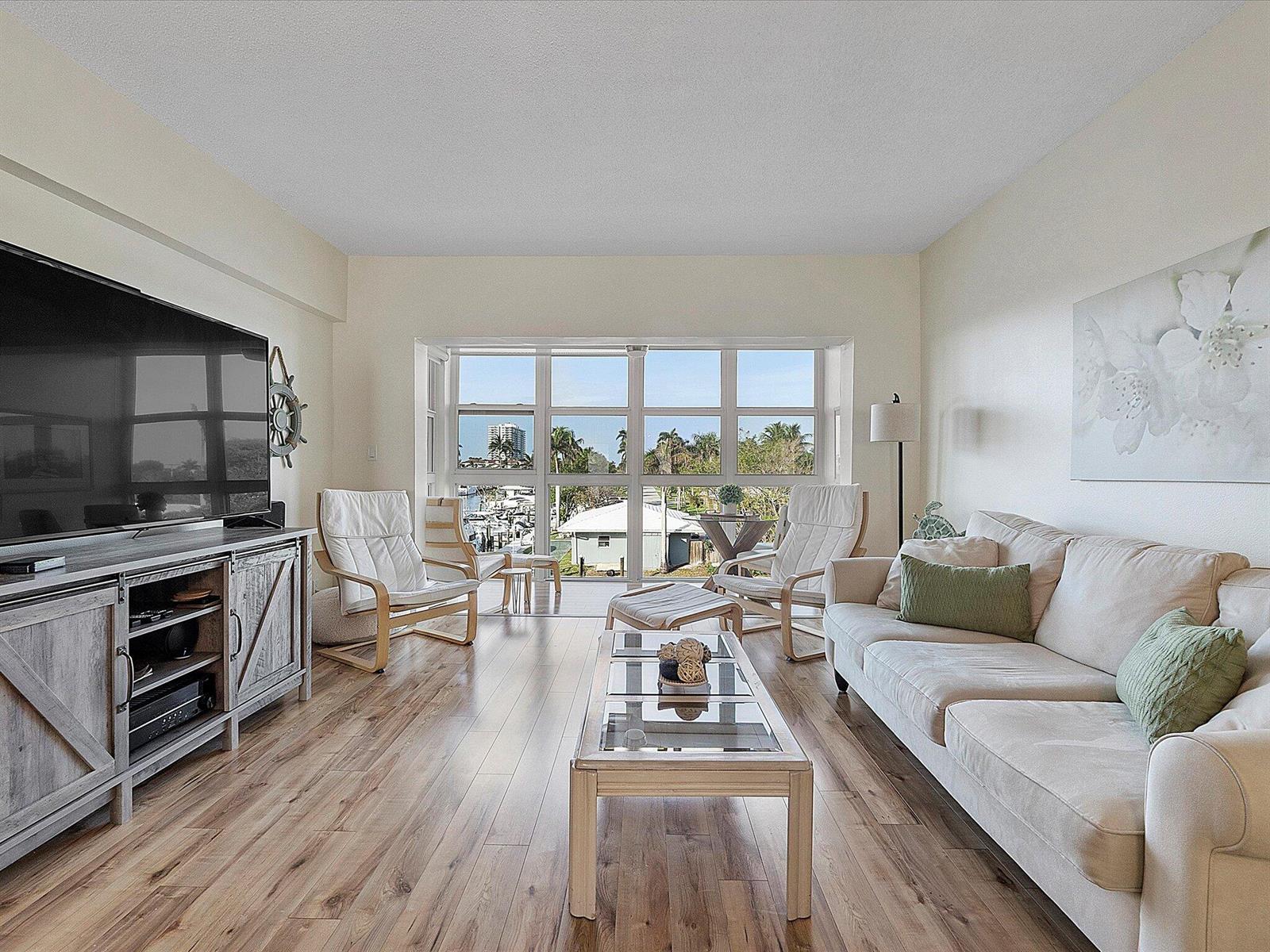A living room with wood-look flooring, a large television, a sofa, and floor-to-ceiling windows — 1481 S Ocean Boulevard # 315a, Pompano Beach FL 33062, POMPANO BEACH, FL