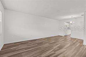 An empty room with white walls and light wood-look flooring leads to a kitchen area — 5257 81ST LANE N UNIT 17, ST PETERSBURG, FL