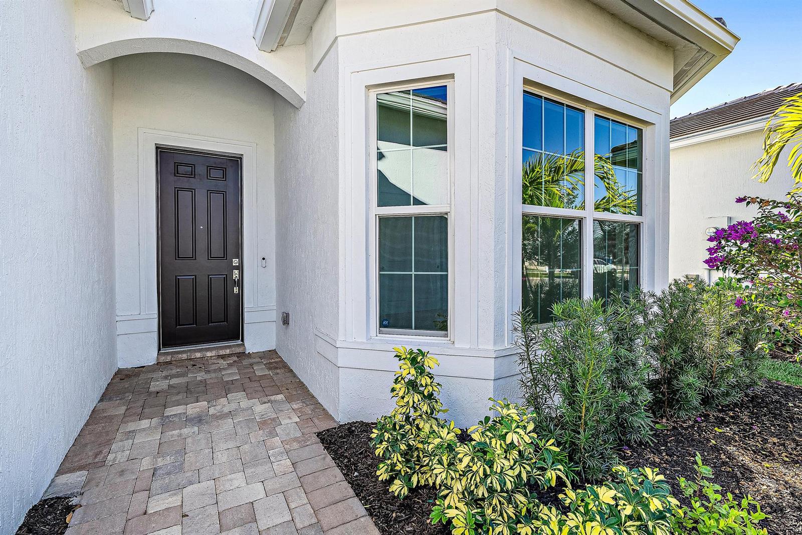 A dark front door sits beside a bay window on a paved entryway — 9775 SW Meridian Way, Stuart FL 34997, STUART, FL