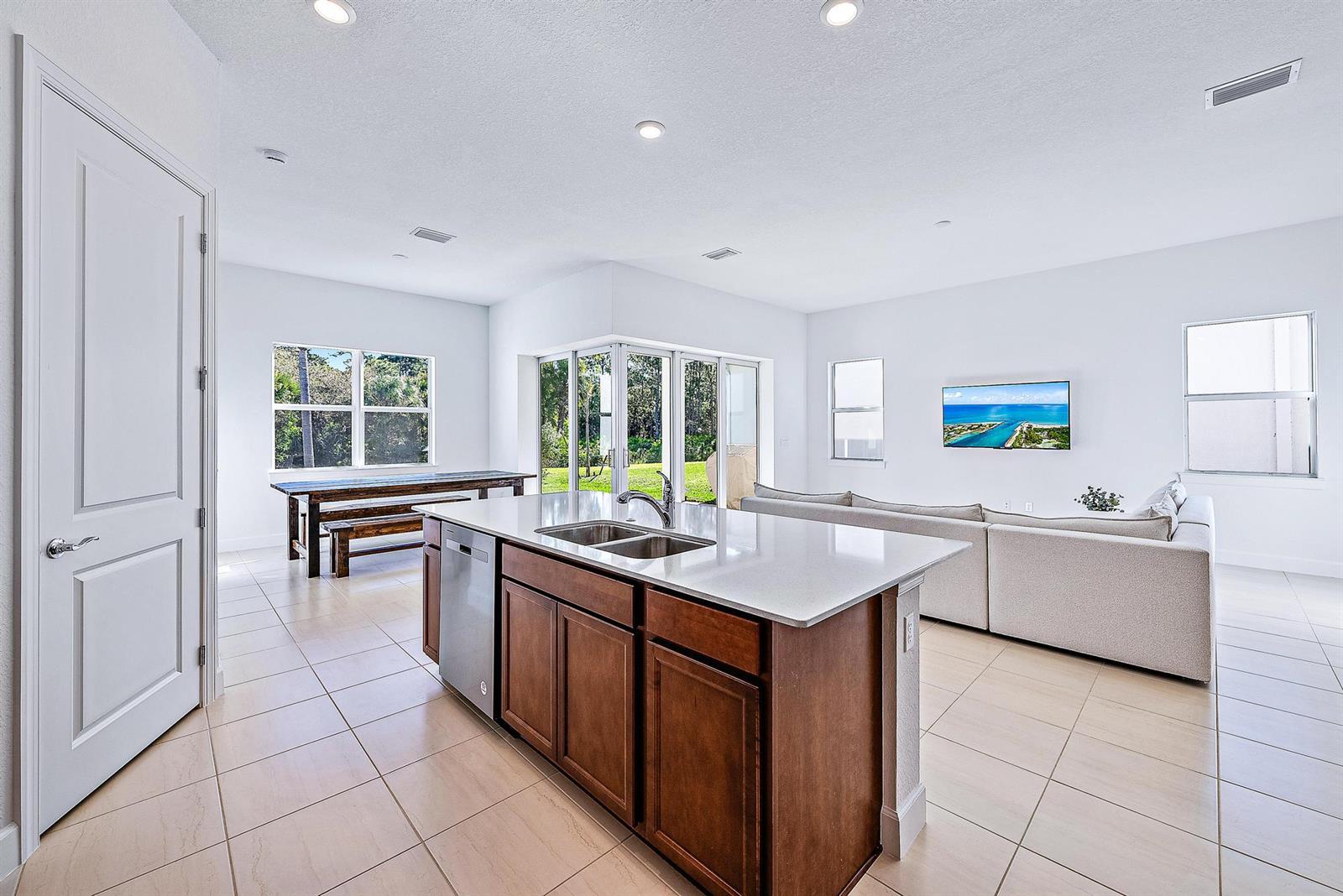 A kitchen island with a sink sits in an open-concept room with tile flooring — 9775 SW Meridian Way, Stuart FL 34997, STUART, FL