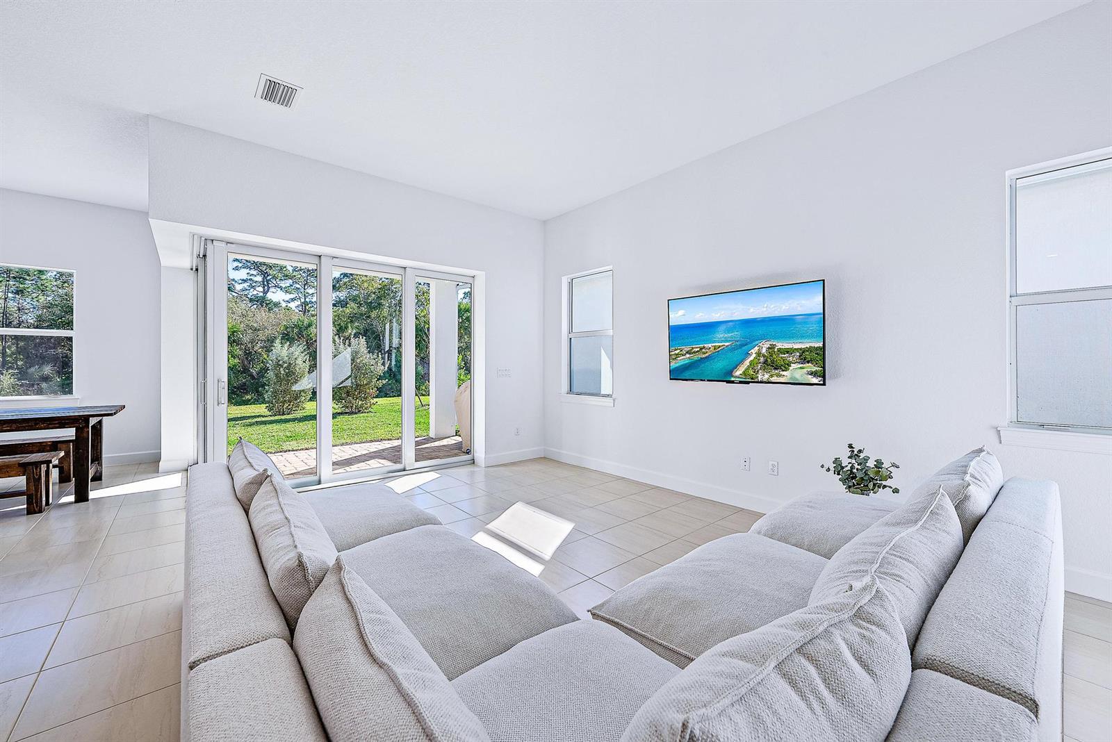 A bright living room features a large sectional sofa, tile flooring, and sliding glass doors — 9775 SW Meridian Way, Stuart FL 34997, STUART, FL
