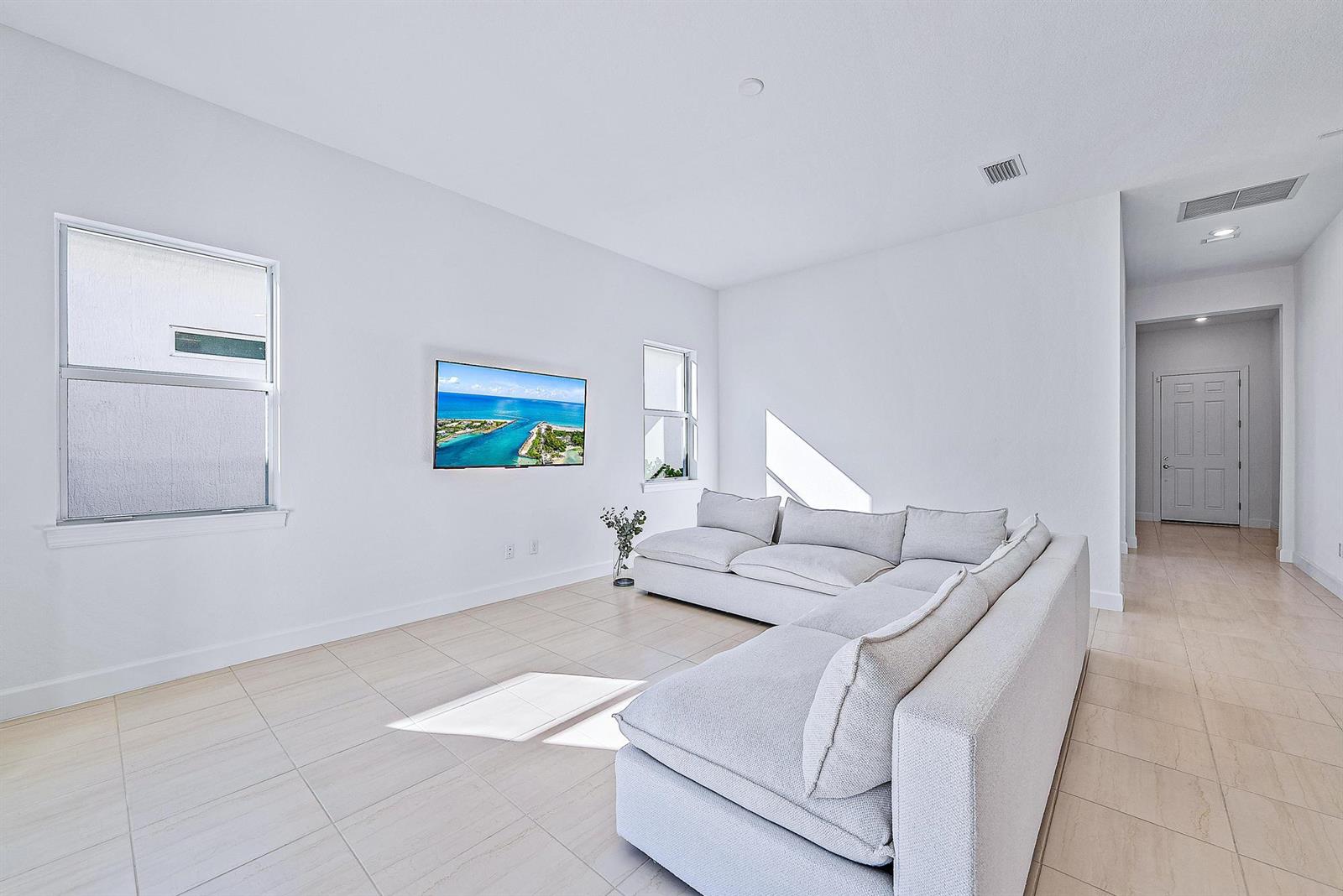 A living room features a light gray sectional sofa, a wall-mounted television, and tile flooring — 9775 SW Meridian Way, Stuart FL 34997, STUART, FL