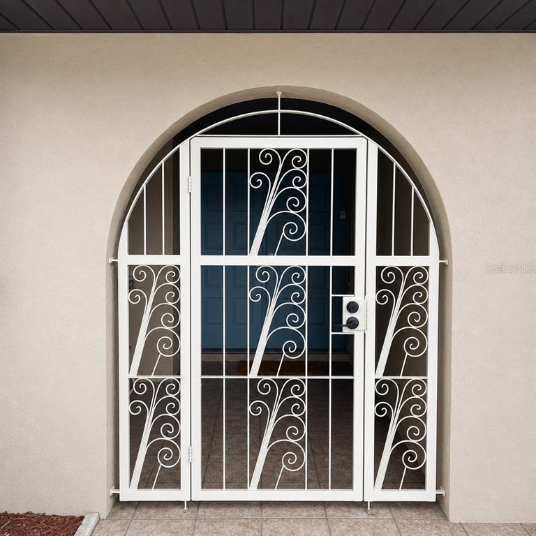 A white metal security gate with decorative scrollwork is installed in an arched entryway — 612 WOOD DRIVE, KISSIMMEE, FL