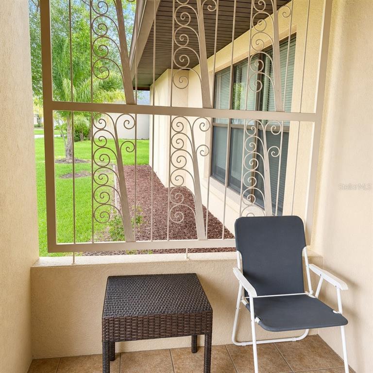 A covered patio features a metal security screen, a small wicker table, and a chair — 612 WOOD DRIVE, KISSIMMEE, FL