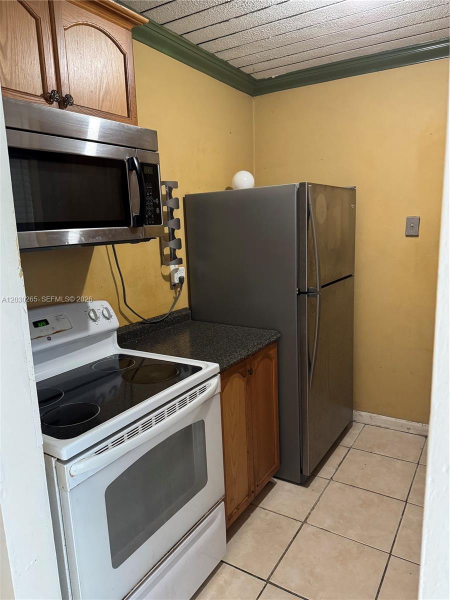A kitchen features a white stove, stainless steel microwave, dark countertop, and a gray refrigerator — 7105 W 13th Ave # 403, Hialeah FL 33014, HIALEAH, FL